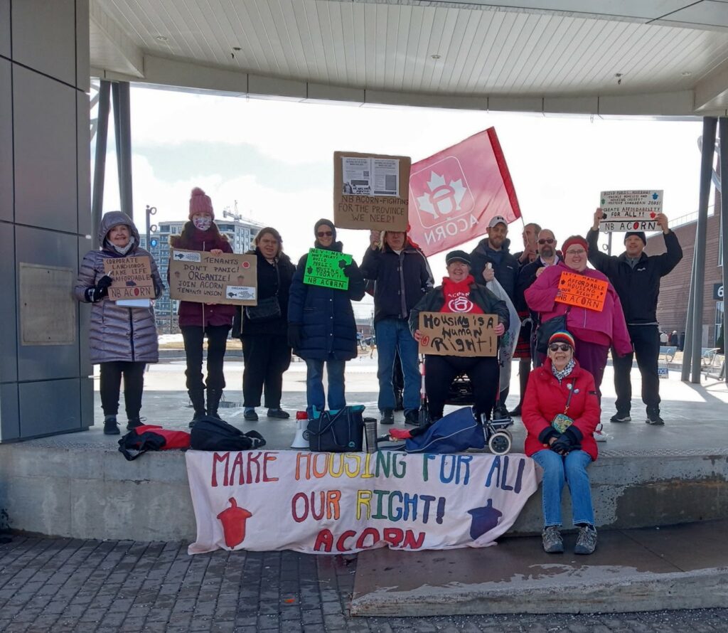 New Brunswick ACORN members in Moncton group photo. Signs read "Make housing for all \ our fight \ ACORN". "Housing is a human right", "Tenants don't panic. Organize!" \ "Corporate landlords make life unaffordable"