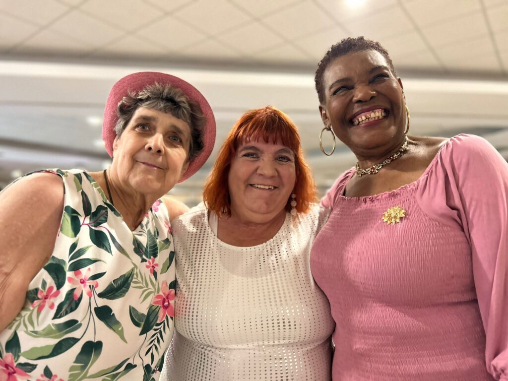 Three women posing closely together, smiling for a selfie indoors.