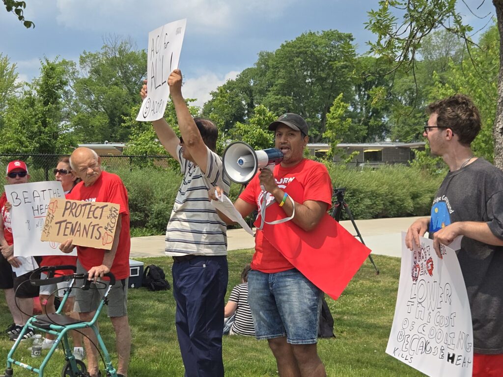 Protesters outdoors holding signs; a man with a megaphone leads the demonstration.