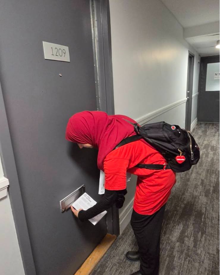 Person in red clothing bending to insert letters into a door mail slot labeled 1209 in a hallway.